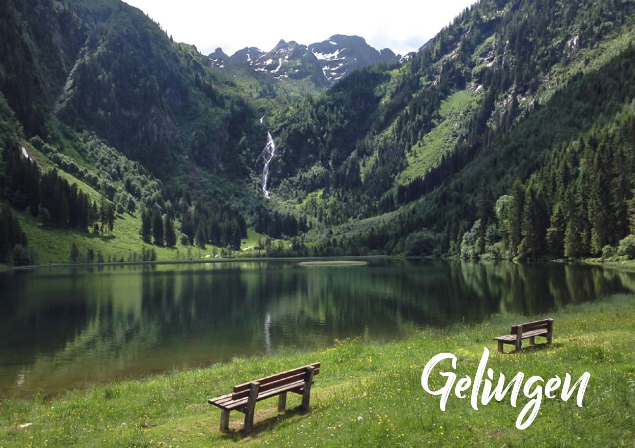 Foto eines Bergsees mit grüner Wiese und zwei Sitzbänken am See. Unten rechts der Schriftzug "Gelingen"