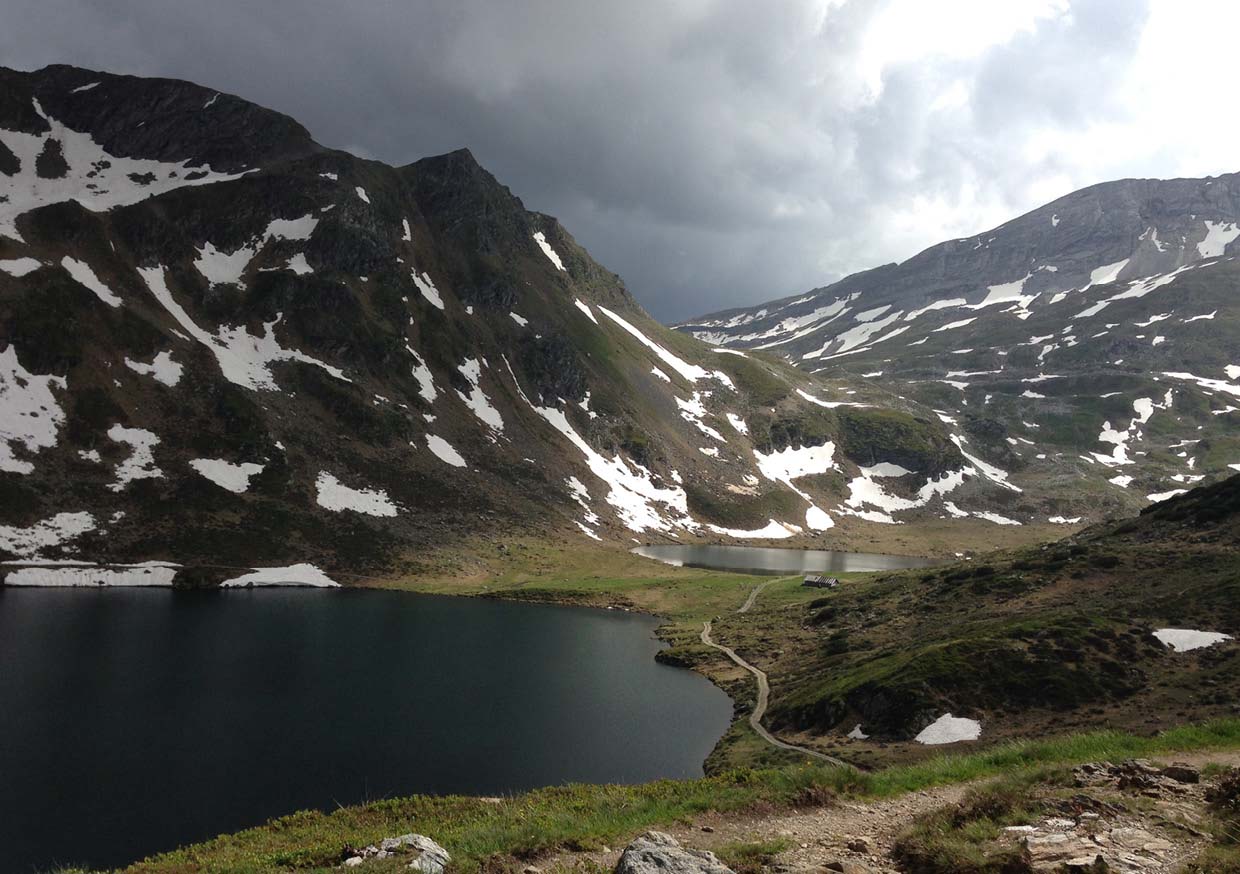 Photo of a mountain lake with snow on the mountains and a dramatic sky.