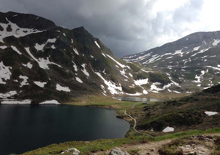 Photo of a mountain lake with snow on the mountains and a dramatic sky.